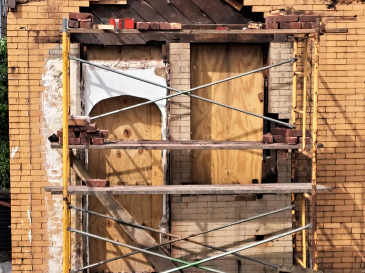 Brick wall opened above a window opening with scaffolding set for the rebuild