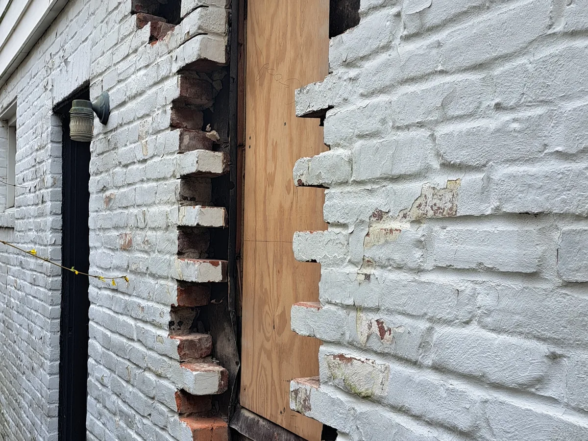 Opening in a painted brick wall bricked back in around a boarded doorway