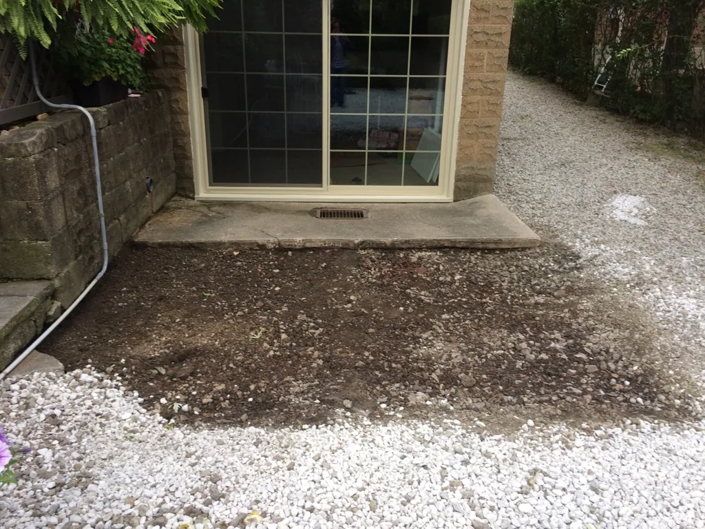Dirt and gravel left where an old concrete patio slab was broken out beside a sliding patio door