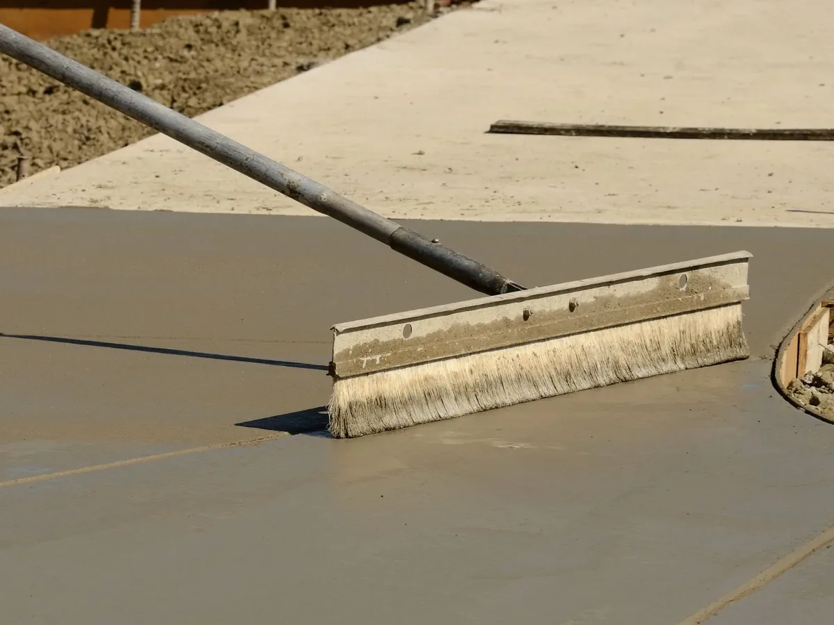 Drawing a broom finish across a freshly placed concrete sidewalk still in its forms