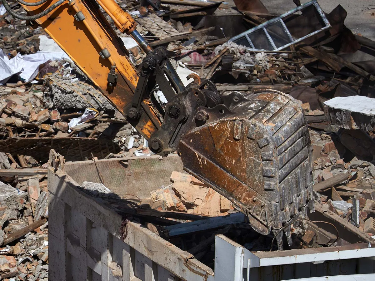Excavator bucket loading brick and masonry debris into a dump truck body
