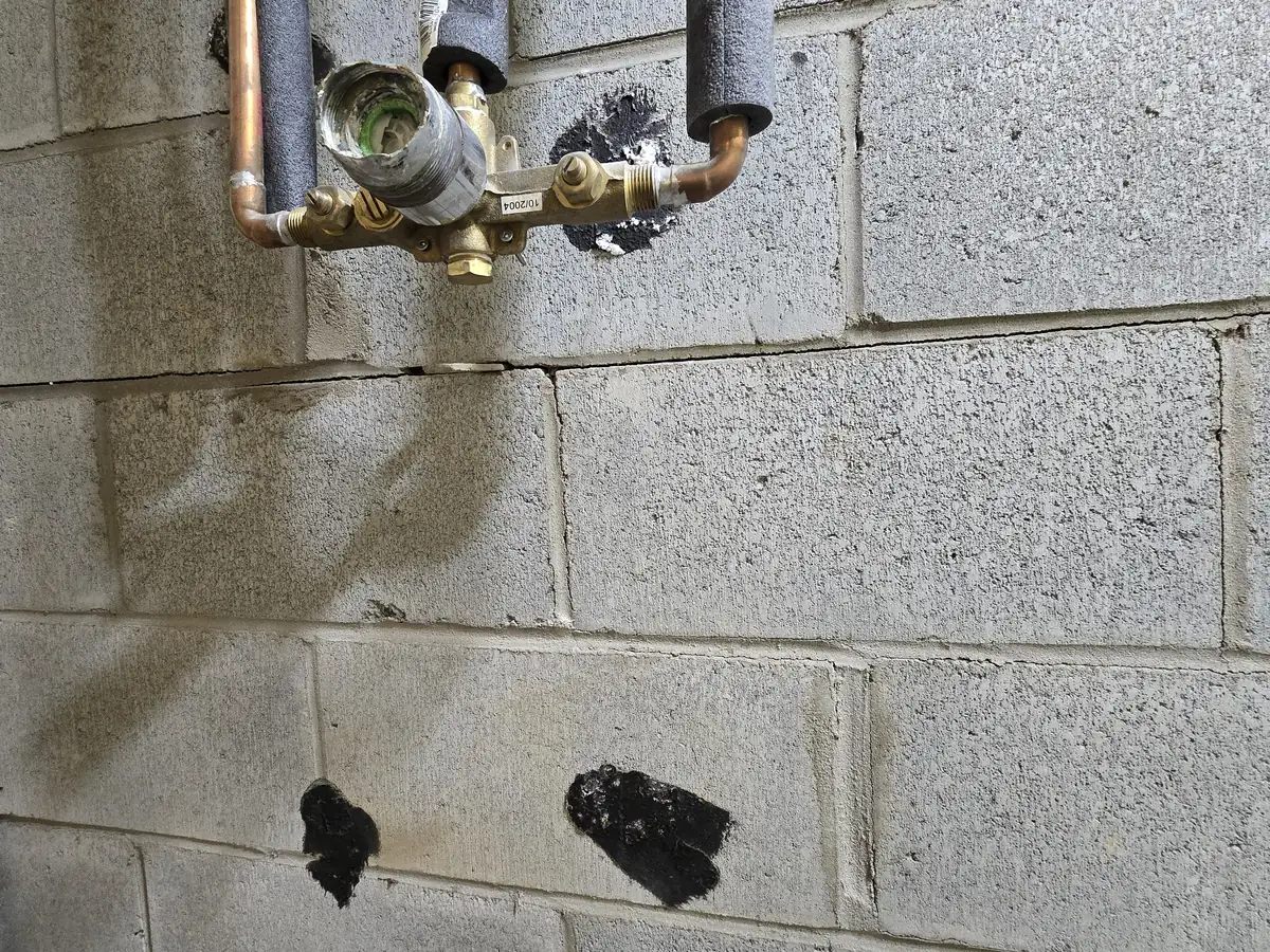Cracked concrete block basement wall with old tar patches over the failed joints