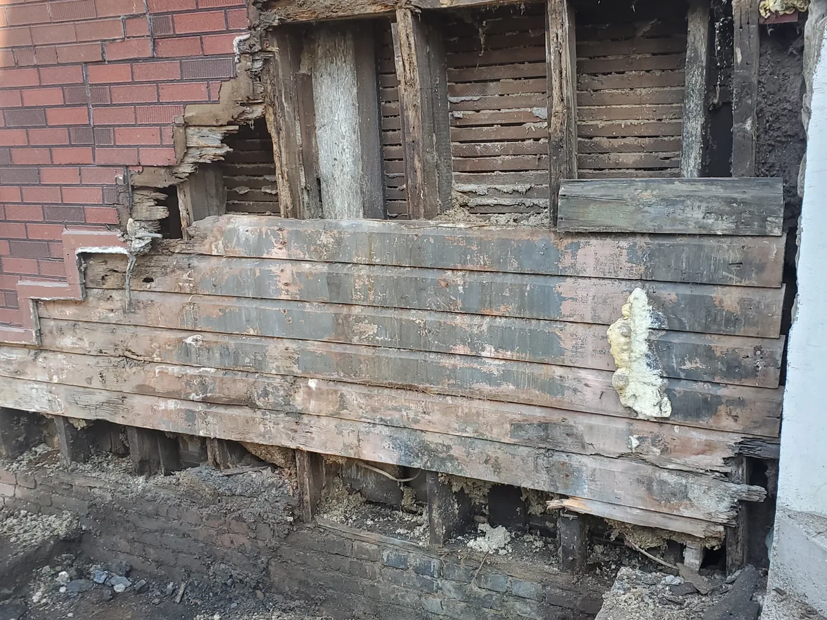 Base of a masonry wall opened up, showing the rotted timber sill behind the brick