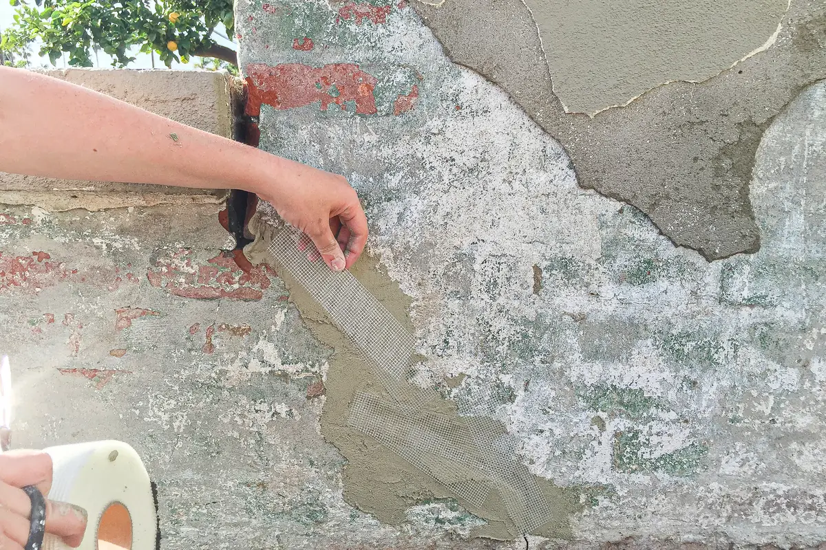 Stucco repair on an old wall: mesh pressed into a fresh base coat where loose stucco came off the brick underneath